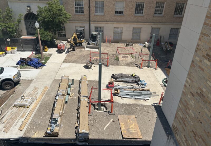 Piles of lumber, other building materials and several work vehicles occupy a building courtyard under construction.