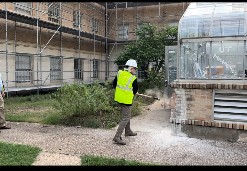 A worker dismantles an aging greenhouse with a sledge hammer in the midst of a courtyard under construction.