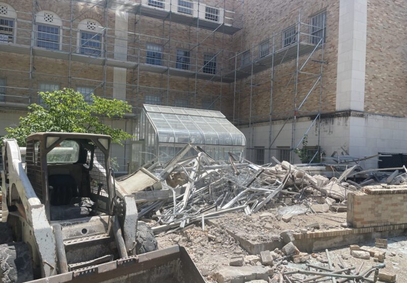 A skid loader vehicle parked next to a pile of rubble in a courtyard under construction
