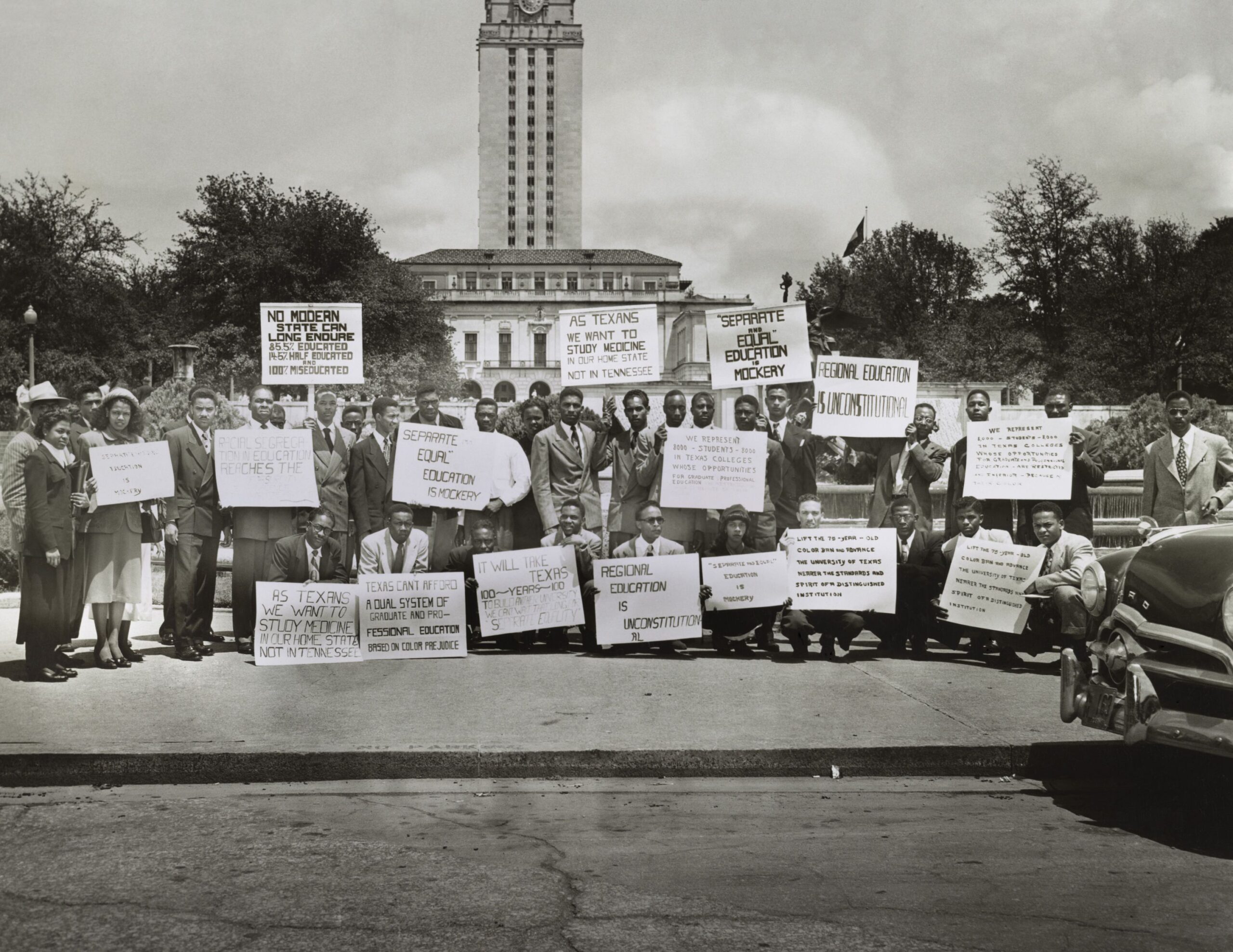 Thirty African Americans in business attire gather to protest state segregation on the steps of the Main Building on the campus of the University of Texas at Austin