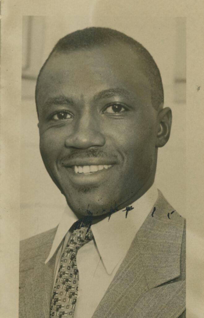 A young man in a jacket and tie smiles at the camera