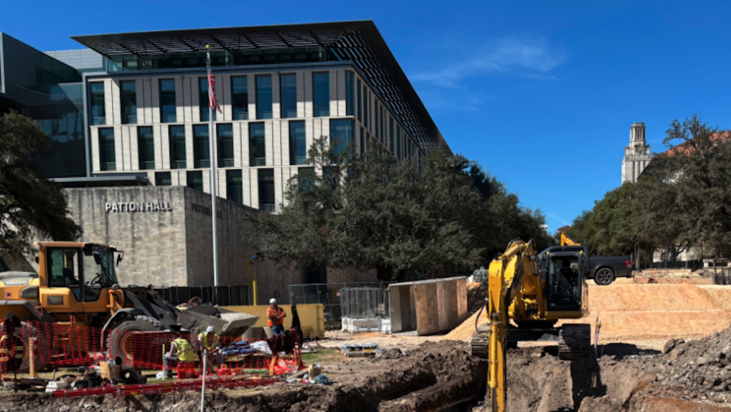 Construction site with two demolition trucks in the foreground. An academic building is in the background.